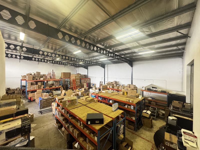 Spacious industrial warehouse area featuring high ceilings with exposed steel trusses, concrete flooring, and extensive built-in metal racking for storage.