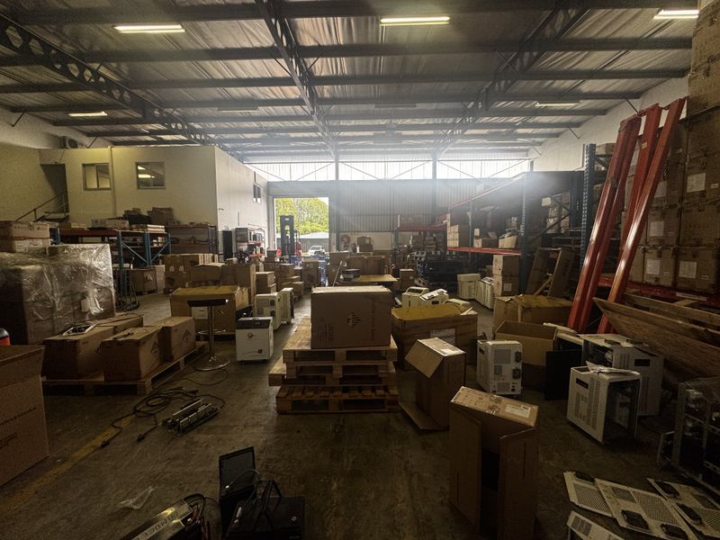 Spacious industrial warehouse featuring high ceilings with exposed steel trusses, concrete flooring, and integrated storage racking with large roller shutter access.