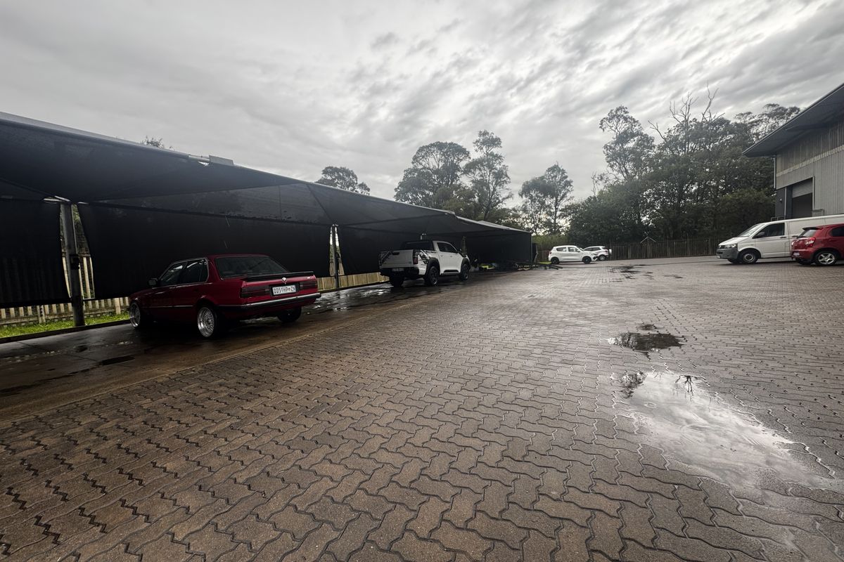 Industrial property exterior featuring a large paved parking area with a covered shade cloth carport structure.
