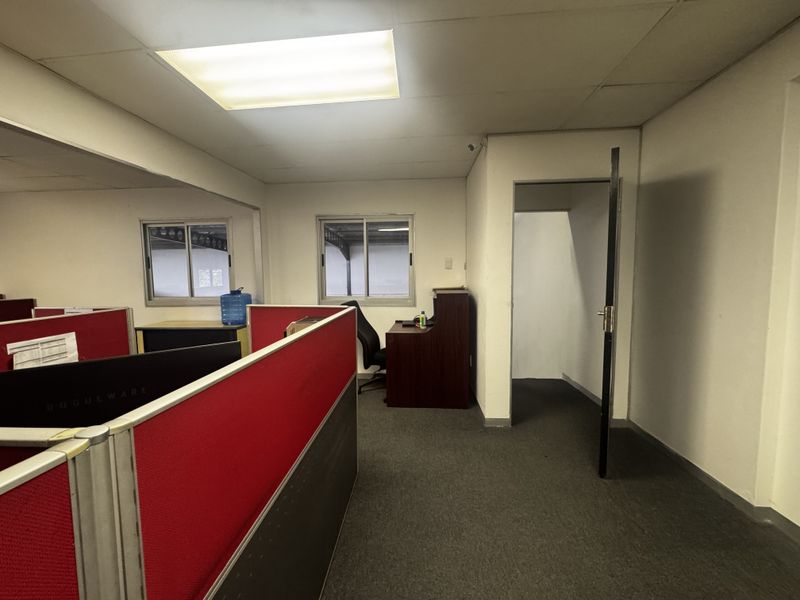 An industrial office space featuring carpeted flooring, drop ceiling with fluorescent lighting, and sliding windows.