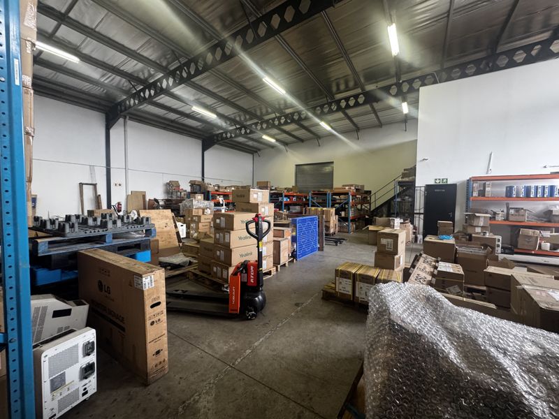 Spacious industrial warehouse unit featuring high ceilings with exposed steel trusses, concrete flooring, and integrated steel racking systems for storage.