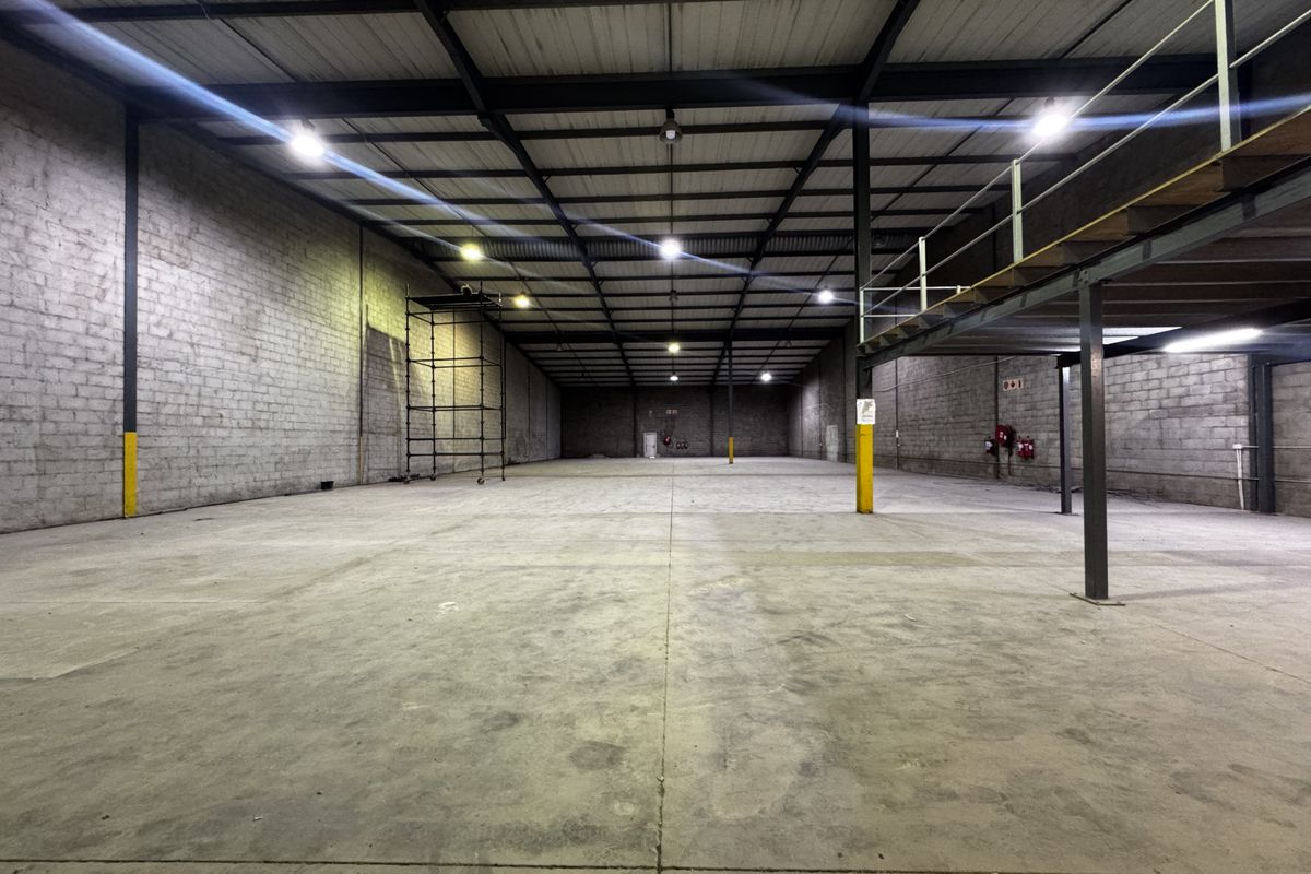 Spacious industrial warehouse featuring high ceilings with exposed steel trusses, concrete flooring, and a mezzanine level, suitable for storage or manufacturing operations.