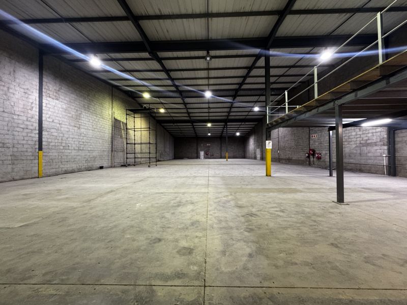 Spacious industrial warehouse featuring high ceilings with exposed steel trusses, concrete flooring, and a mezzanine level, suitable for storage or manufacturing operations.