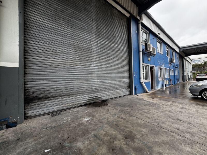Industrial property exterior featuring a large roller shutter door, concrete driveway, and wall-mounted air conditioning units on a blue painted facade.