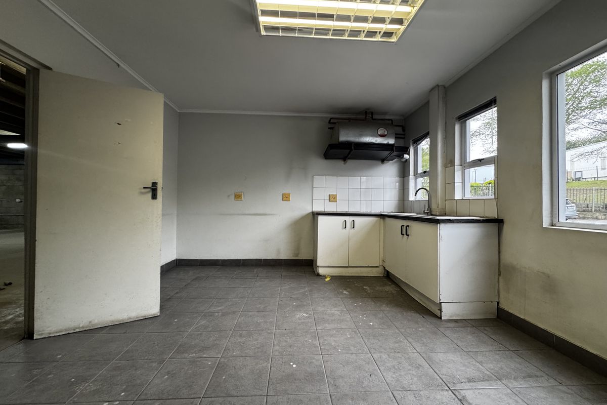 A functional industrial kitchen space featuring tiled flooring, built-in base cabinetry, a stainless steel sink, and an extractor fan, requiring cosmetic updates.