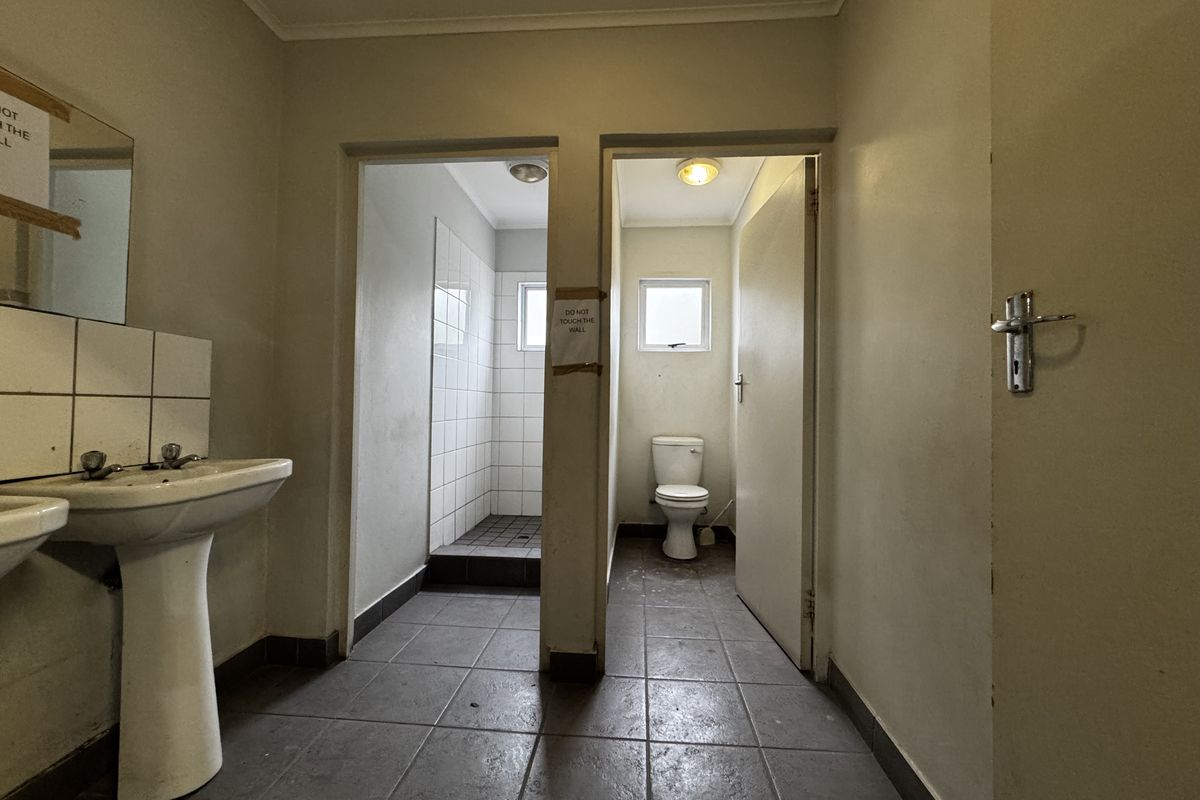 Functional industrial bathroom facility featuring a pedestal basin, separate shower cubicle, and a private toilet stall with tiled flooring.
