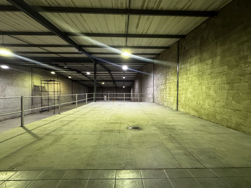 Spacious industrial mezzanine area featuring exposed steel roof trusses, concrete block walls, and functional overhead lighting, suitable for storage or workshop use.