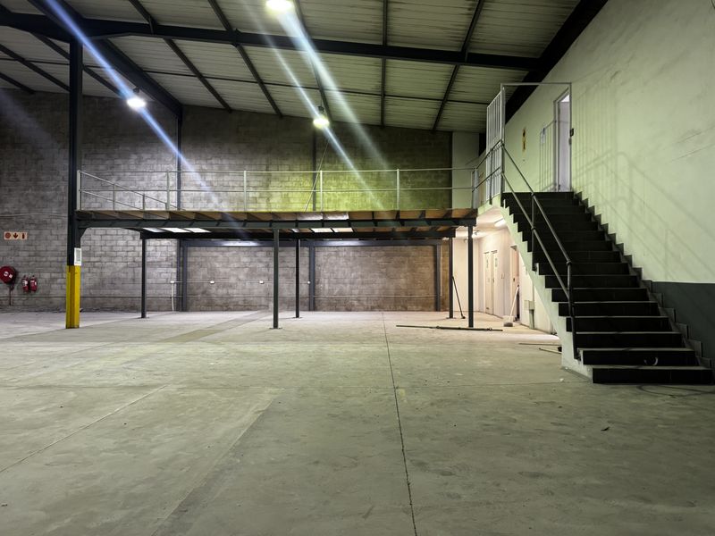 Spacious industrial warehouse unit featuring a mezzanine level, steel staircase, concrete flooring, and exposed structural elements, suitable for storage or light manufacturing operations.
