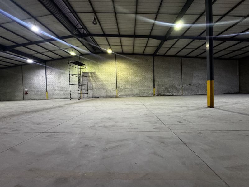 Spacious industrial warehouse unit featuring high ceilings with exposed steel trusses, concrete flooring, and durable brick wall construction.