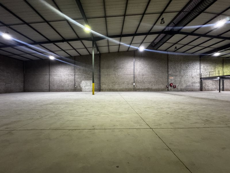 Spacious industrial warehouse featuring high ceilings, exposed steel trusses, durable concrete flooring, and a mezzanine level, suitable for storage or manufacturing operations.