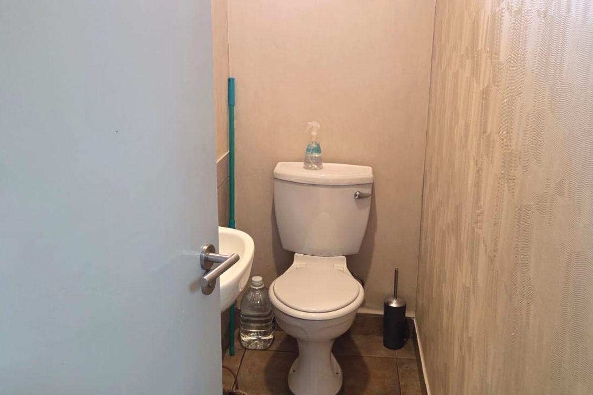 A compact office restroom featuring a standard toilet, wall-mounted basin, tiled flooring, and textured wallpaper finish.