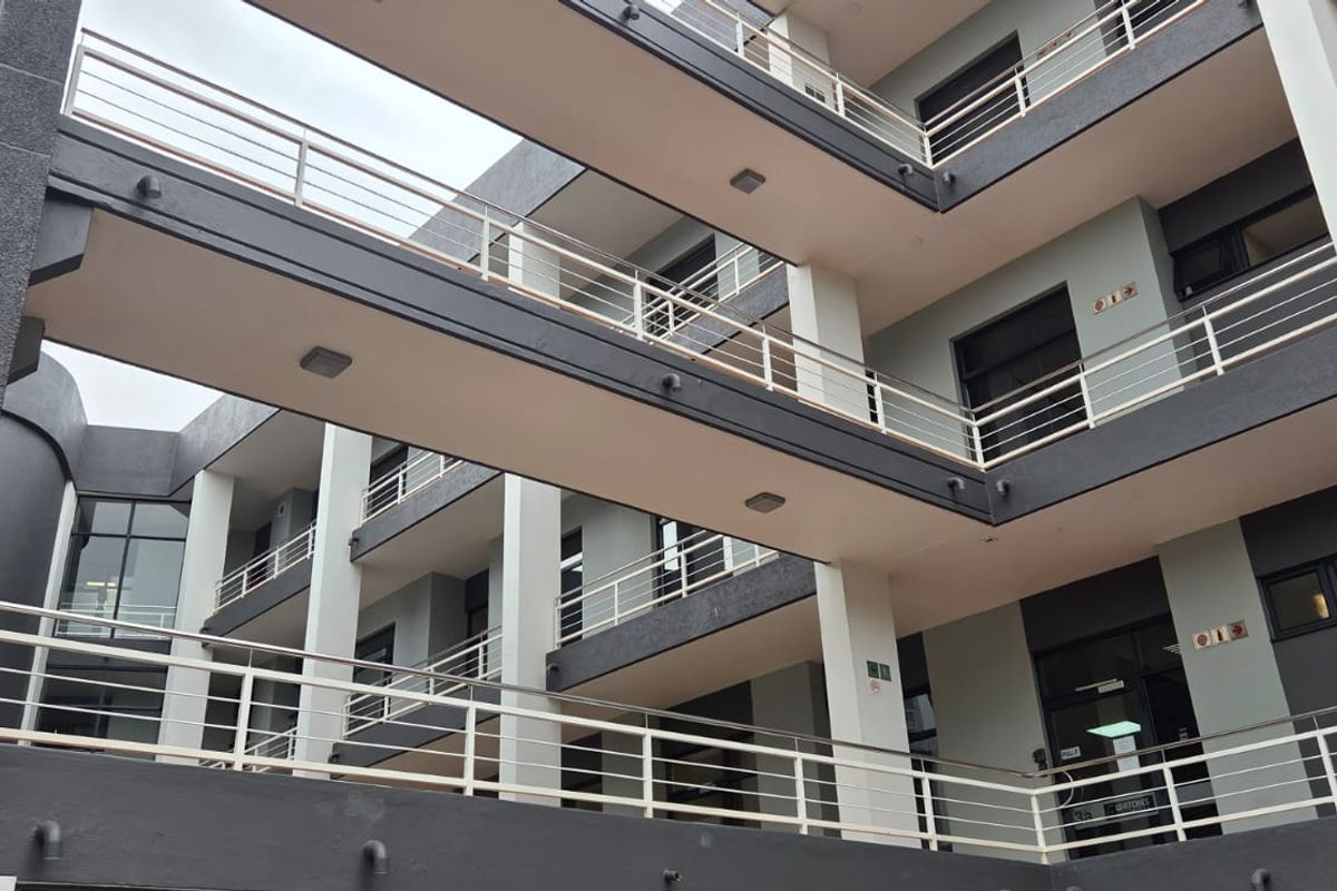 A modern multi-story office building exterior featuring tiered walkways with metal railings and concrete structural pillars.
