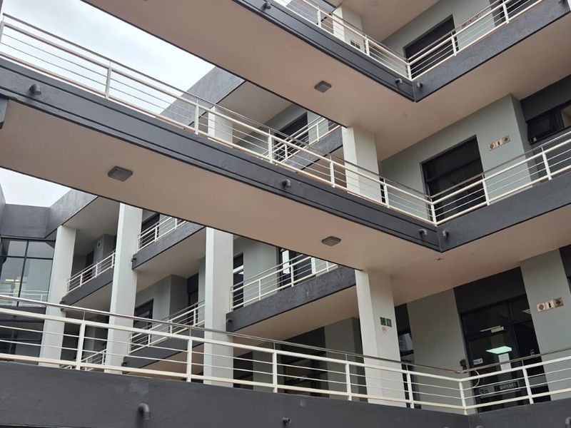 A modern multi-story office building exterior featuring tiered walkways with metal railings and concrete structural pillars.