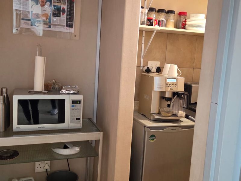 A compact scullery or kitchenette area featuring tiled splashbacks, wall-mounted shelving, and dedicated space for small appliances.