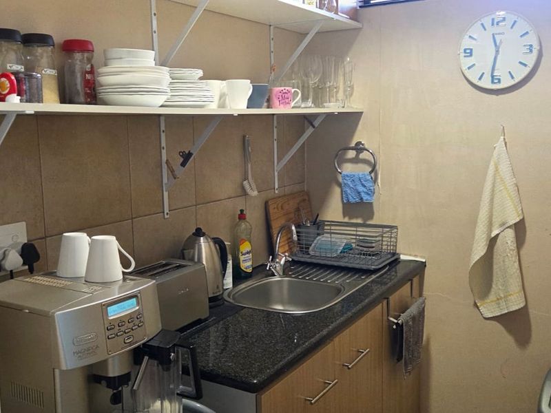 A compact scullery area featuring a stainless steel sink, granite countertop, tiled backsplash, and practical open shelving for storage.