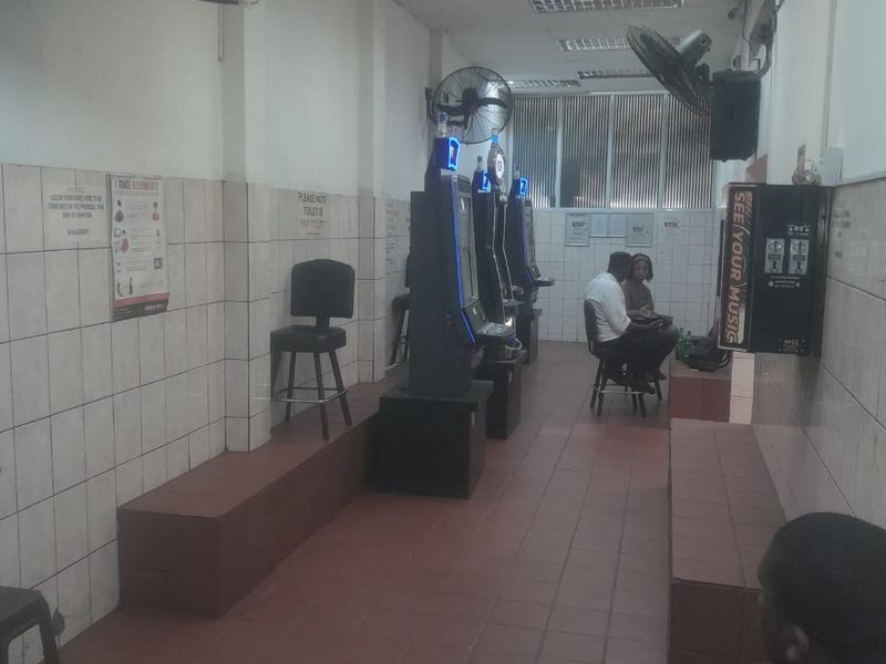 A commercial gaming area featuring tiled flooring, wall-mounted fans, and a suspended ceiling, currently set up with gaming machines and seating.