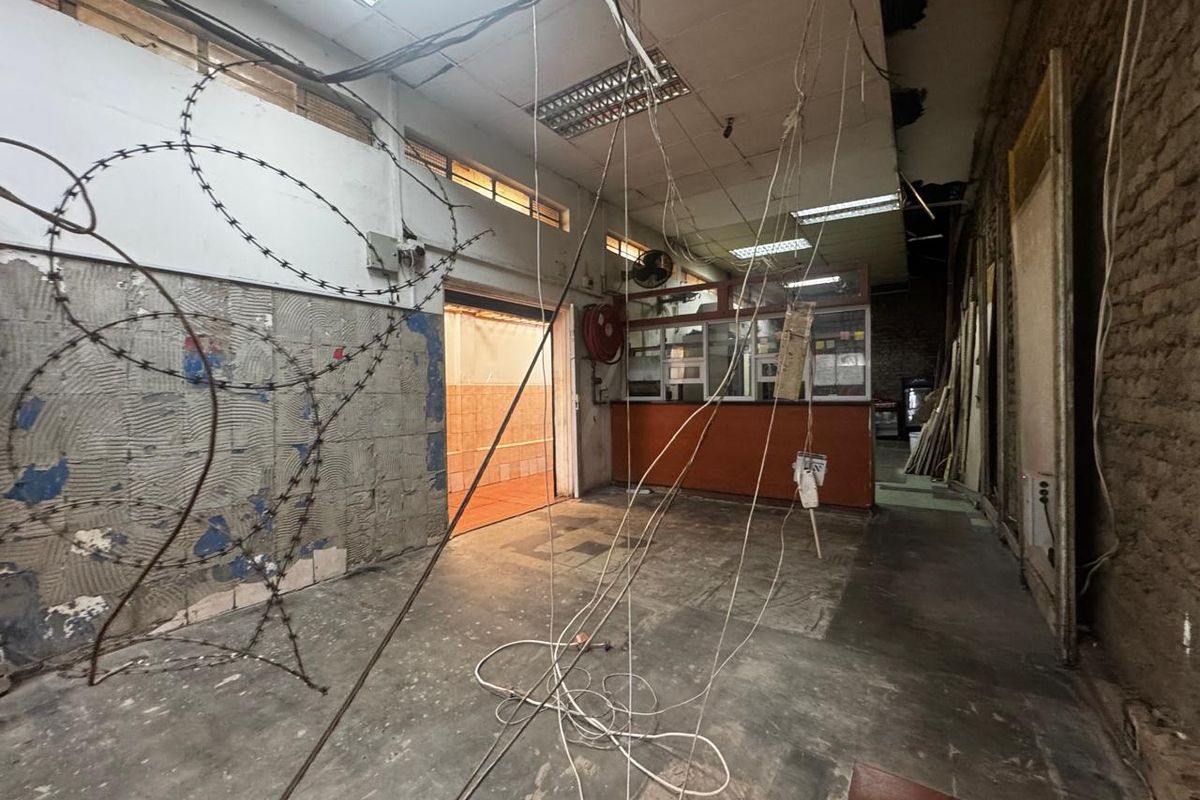 A vacant retail utility space featuring a service counter, exposed brickwork, and damaged ceiling infrastructure requiring significant renovation and repair.