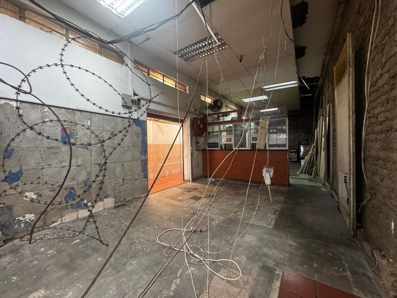 A vacant retail utility space featuring a service counter, exposed brickwork, and damaged ceiling infrastructure requiring significant renovation and repair.