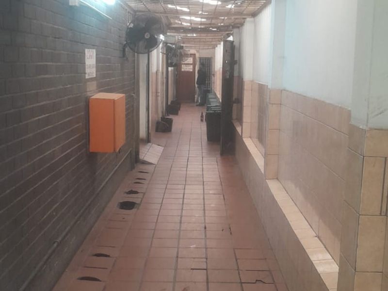 A narrow utility corridor featuring tiled flooring, brick walls, and a corrugated roof structure, suitable for service access or storage.