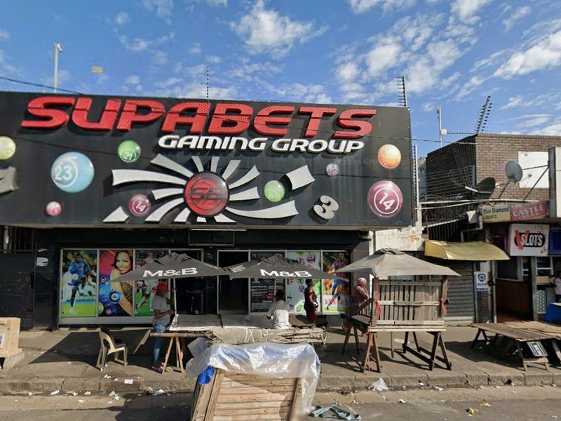 Front elevation of a retail gaming facility featuring prominent branding, glass storefront, and security fencing along the street frontage.