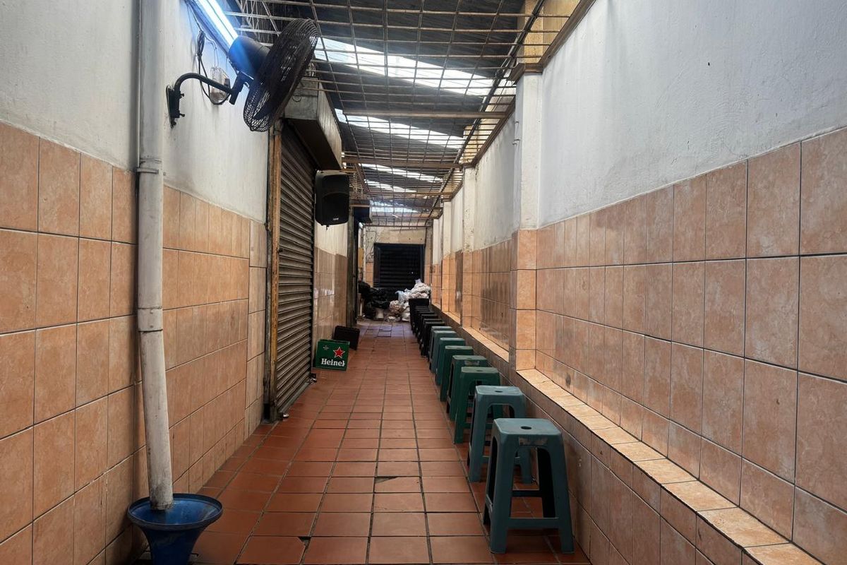 A narrow, covered outdoor walkway or patio area featuring tiled walls and flooring, with a corrugated roof and wall-mounted fan.