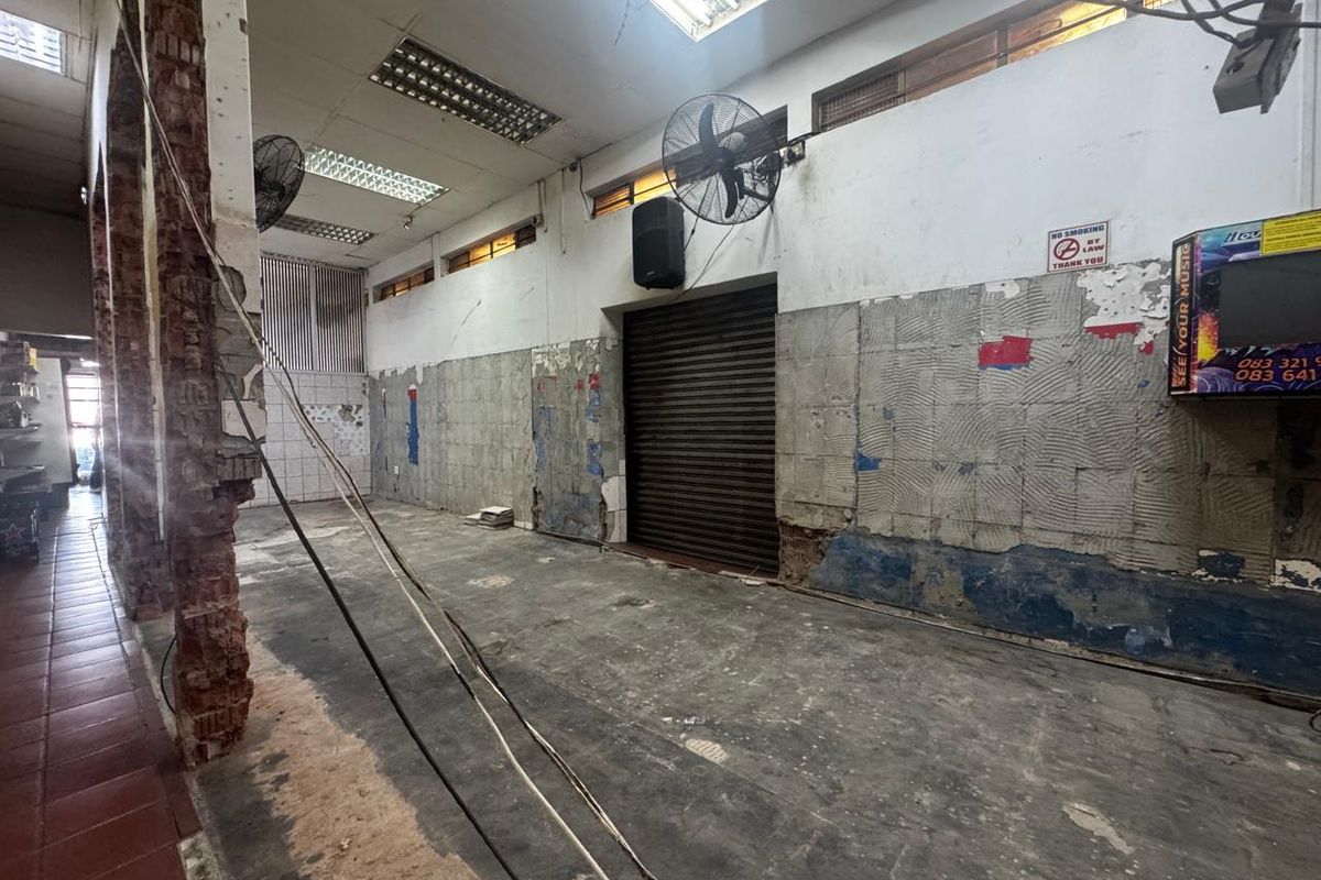 An open-plan utility or retail space featuring a roller shutter door, industrial wall fans, and exposed brickwork, currently in need of significant renovation.