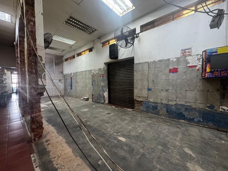 An open-plan utility or retail space featuring a roller shutter door, industrial wall fans, and exposed brickwork, currently in need of significant renovation.