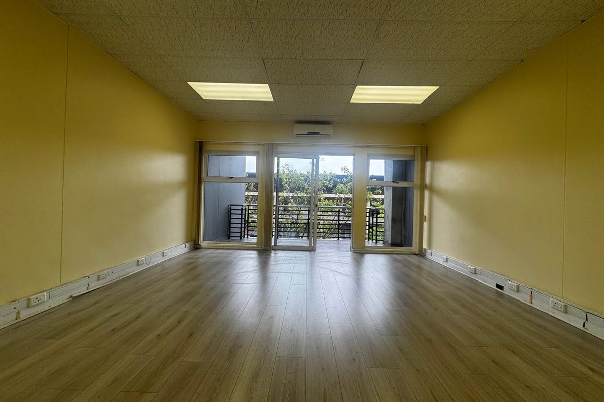 An empty office space featuring laminate flooring, a drop ceiling with recessed lighting, a split-system air conditioner, and sliding glass doors leading to a balcony.
