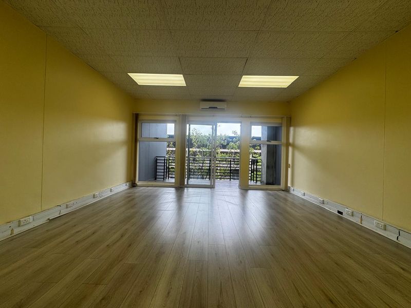 An empty office space featuring laminate flooring, a drop ceiling with recessed lighting, a split-system air conditioner, and sliding glass doors leading to a balcony.