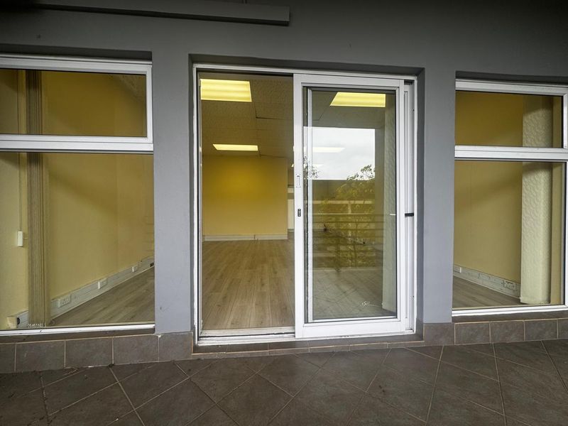 An exterior view of an office space featuring large glass windows, a sliding door, laminate flooring, and a drop ceiling with recessed lighting.