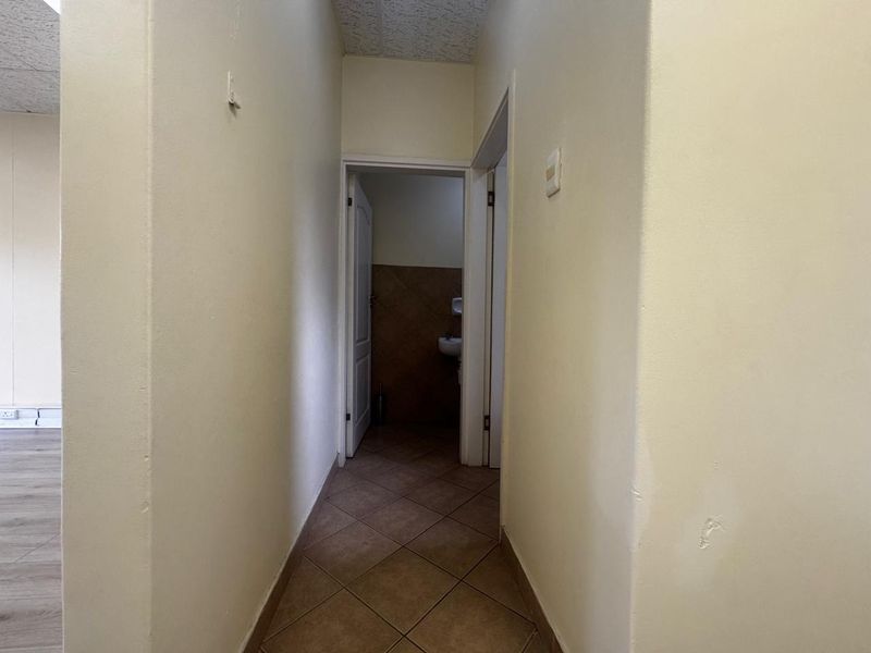 A functional office hallway with tiled flooring and access to adjacent rooms, featuring neutral wall finishes and a drop ceiling.