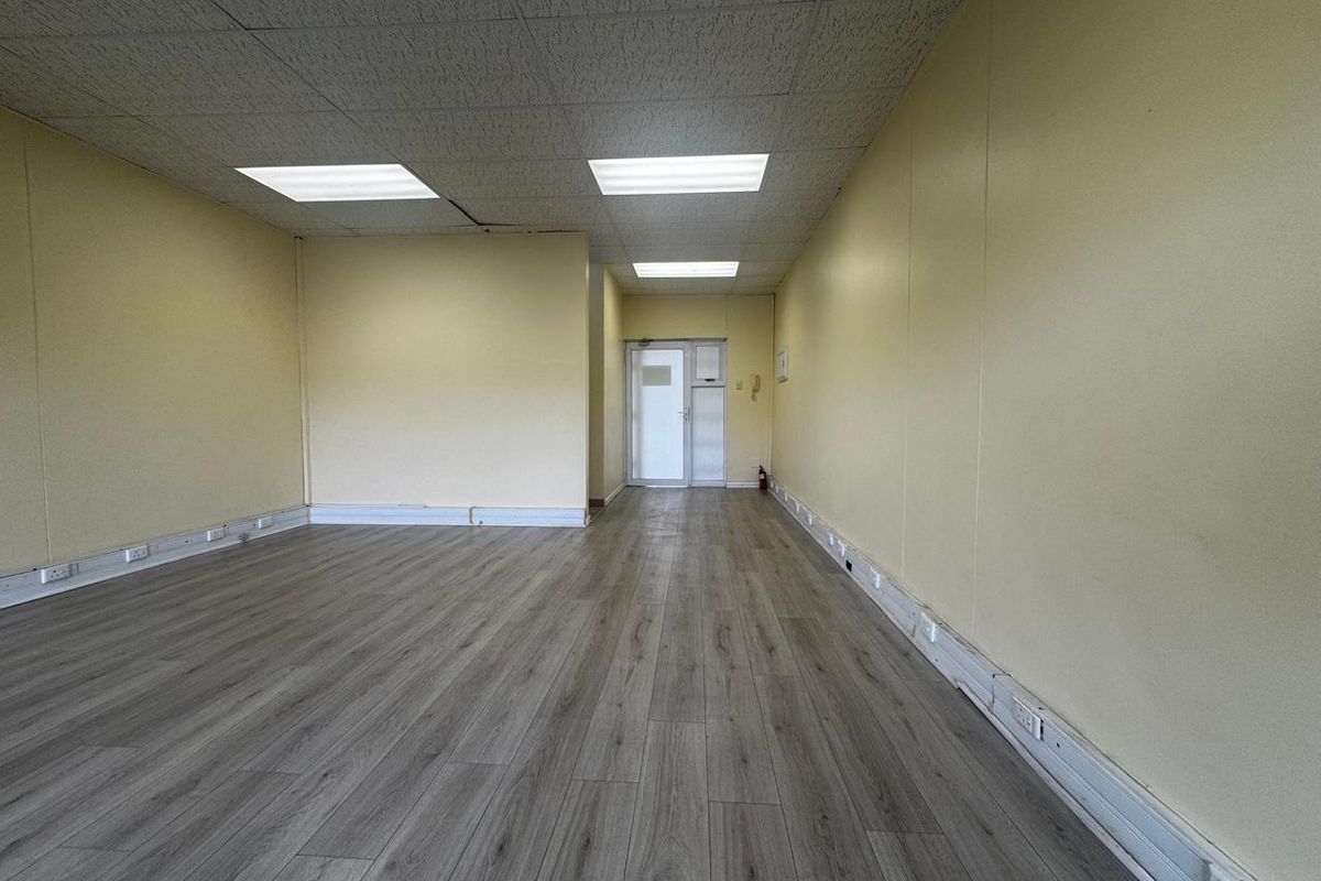 An empty, open-plan office space featuring laminate flooring, suspended ceiling with recessed lighting, and perimeter trunking for electrical connectivity.