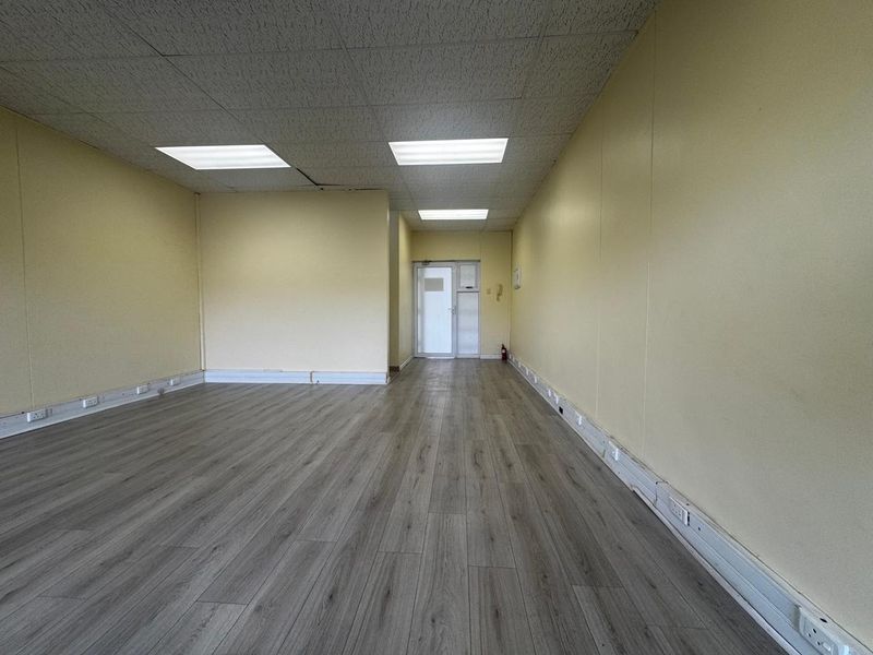 An empty, open-plan office space featuring laminate flooring, suspended ceiling with recessed lighting, and perimeter trunking for electrical connectivity.