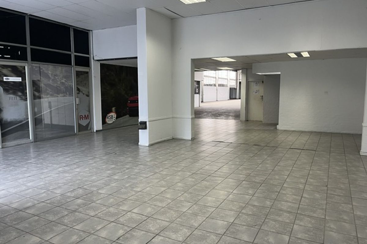 Spacious open-plan industrial unit featuring tiled flooring, suspended ceilings with recessed lighting, and large glass storefront windows, offering a versatile layout for business operations.