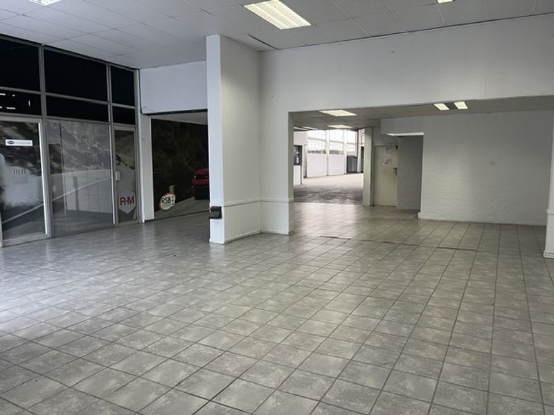 Spacious open-plan industrial unit featuring tiled flooring, suspended ceilings with recessed lighting, and large glass storefront windows, offering a versatile layout for business operations.