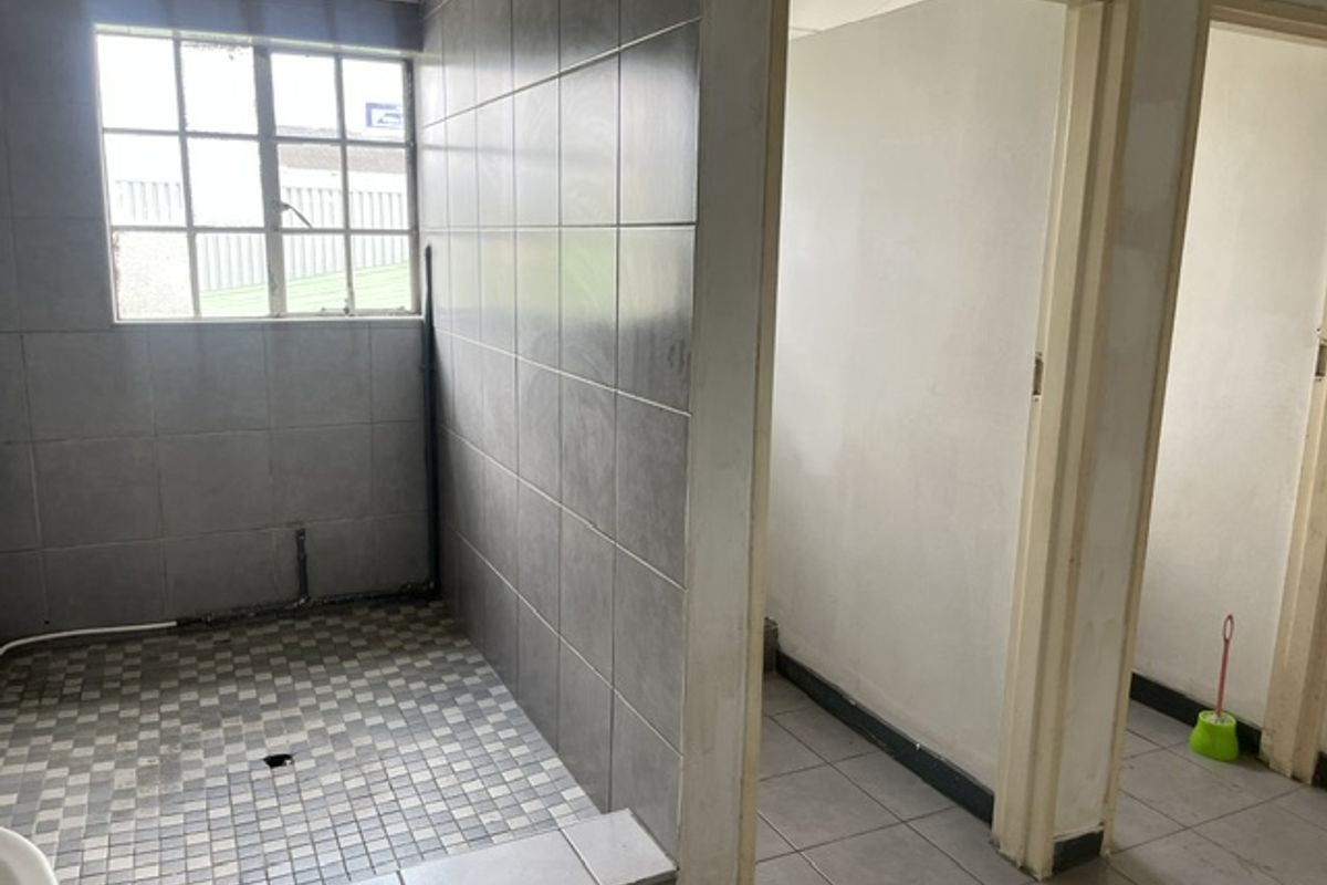 An industrial-style bathroom space featuring grey wall tiles, mosaic floor tiling, and multiple doorways, currently requiring plumbing fixture installation and finishing work.