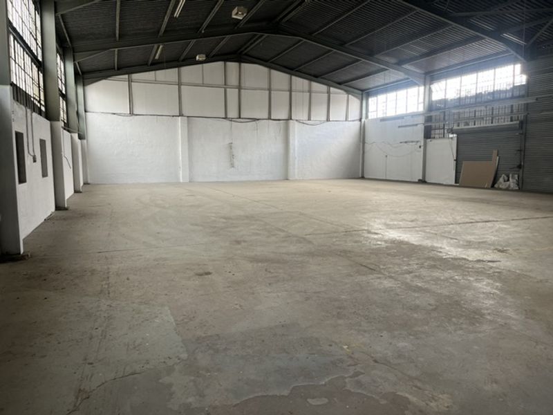 Spacious industrial warehouse unit featuring high ceilings, exposed steel roof trusses, concrete flooring, and large windows providing ample natural light.