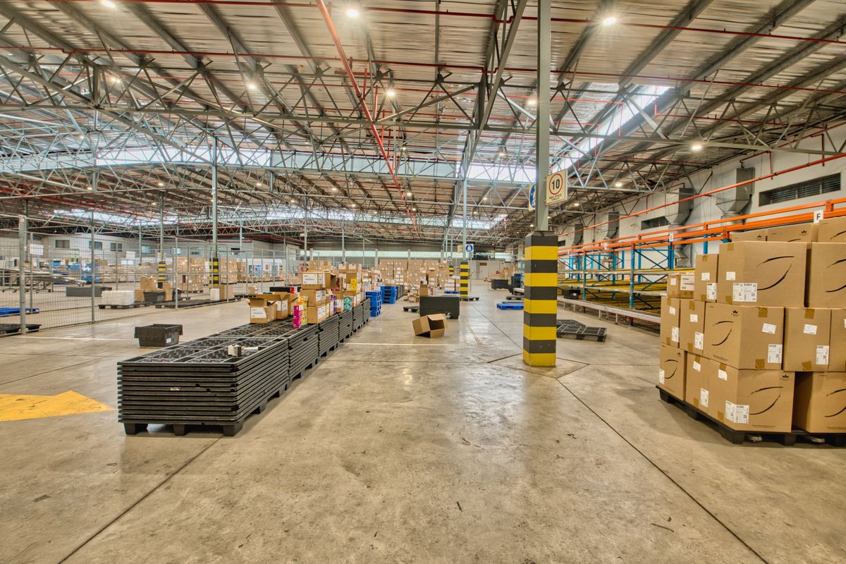 Spacious industrial warehouse facility featuring high exposed steel truss ceilings, durable concrete flooring, and integrated metal racking systems for storage.