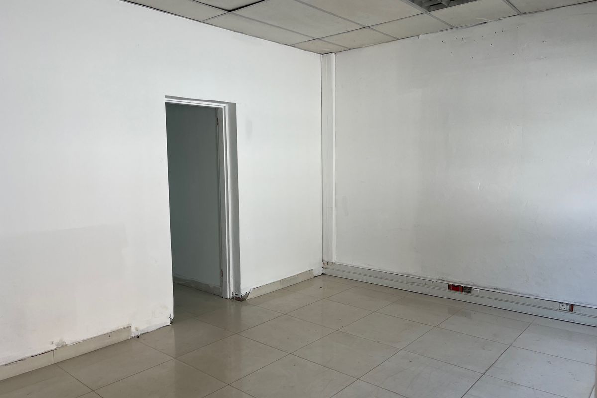 An empty office space featuring tiled flooring, a suspended ceiling with recessed lighting, and perimeter electrical trunking.