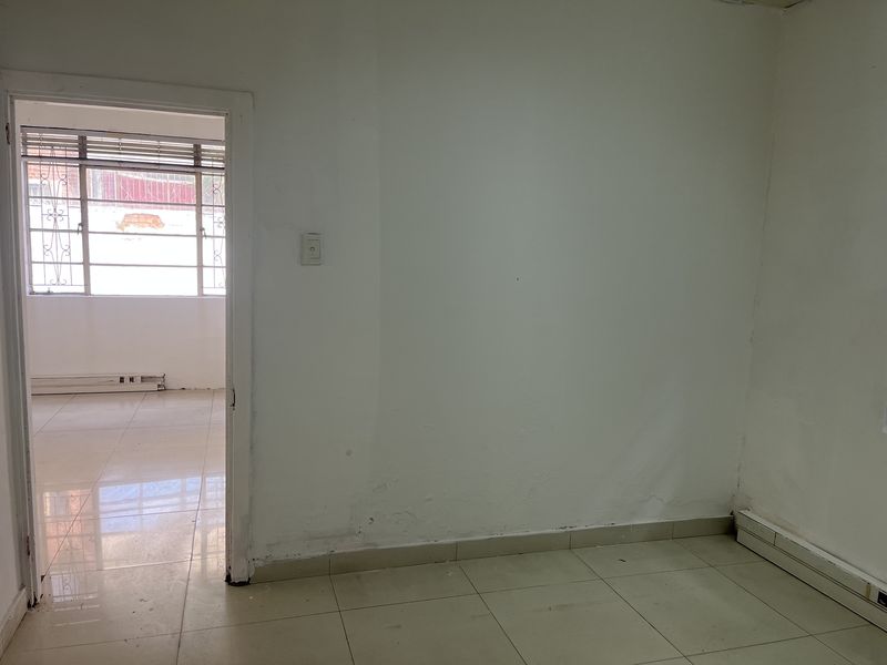 An empty office space featuring tiled flooring and baseboard heating, with a doorway leading to an adjacent room with large windows.