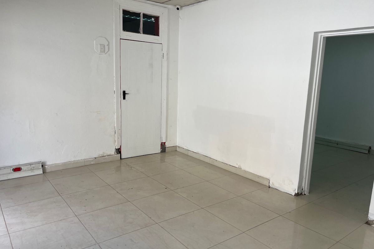 An empty office space featuring tiled flooring, a suspended ceiling, and a white internal door with a transom window.
