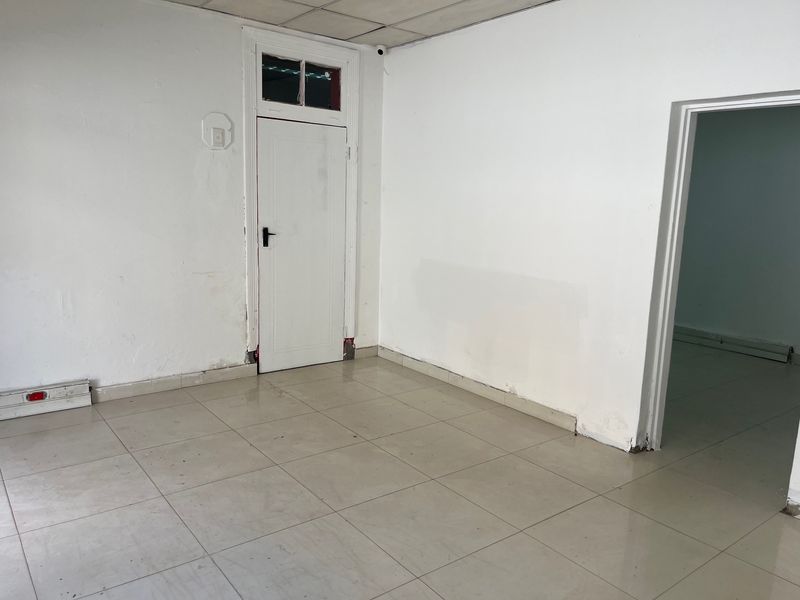 An empty office space featuring tiled flooring, a suspended ceiling, and a white internal door with a transom window.