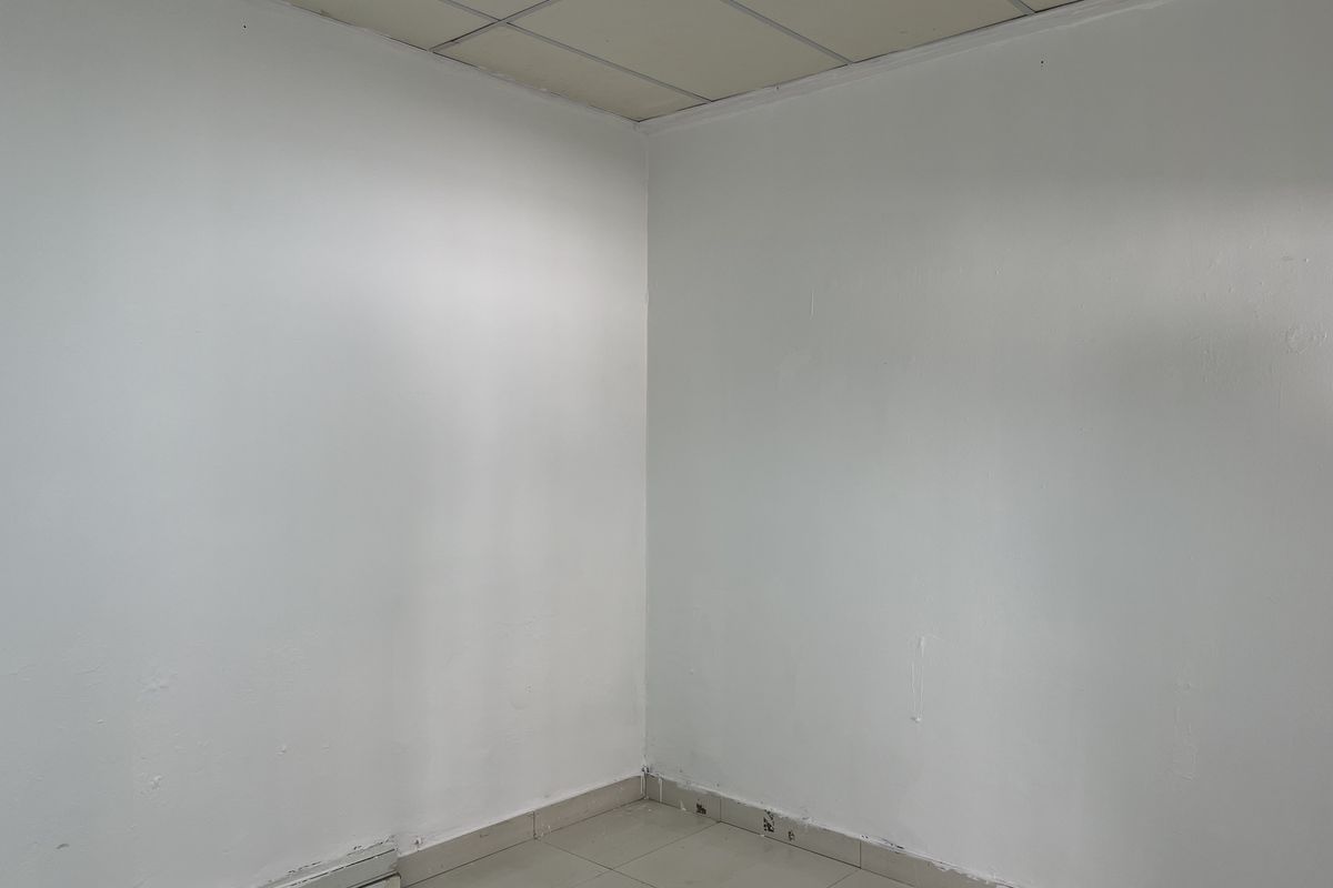A vacant office space featuring neutral white walls, ceramic floor tiles, and a suspended ceiling, ready for customization.