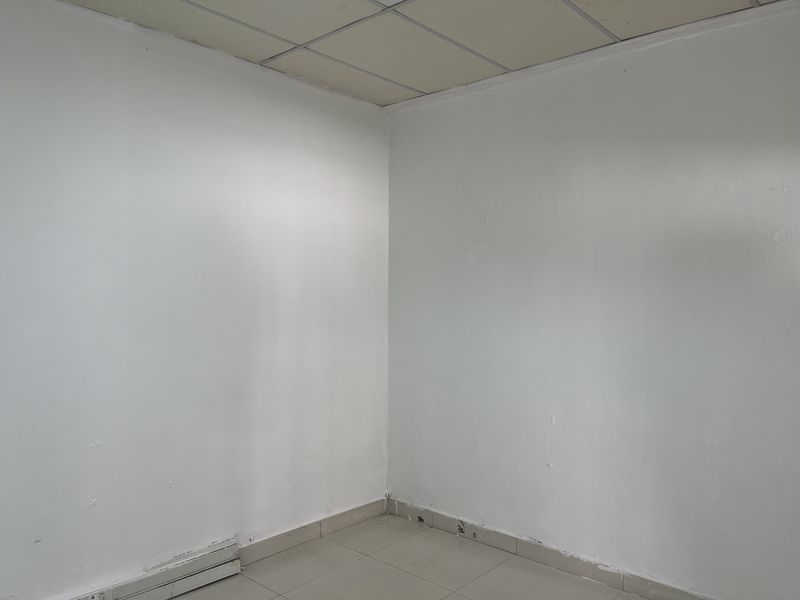 A vacant office space featuring neutral white walls, ceramic floor tiles, and a suspended ceiling, ready for customization.