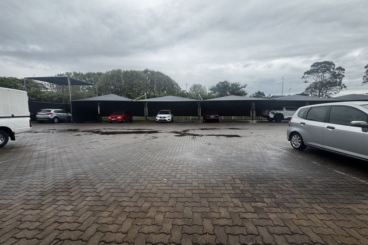 Industrial exterior parking area featuring multiple covered shade cloth carports and paved ground surface.