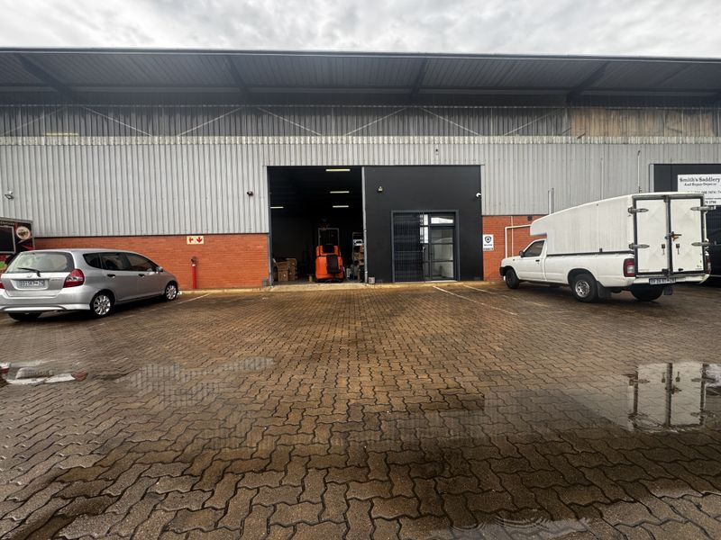Industrial warehouse exterior featuring a brick and corrugated metal facade with a large roller shutter entrance and paved parking area.
