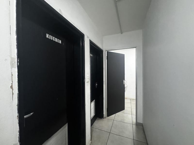 A functional industrial hallway featuring tiled flooring and multiple internal access doors leading to various utility and kitchen spaces.