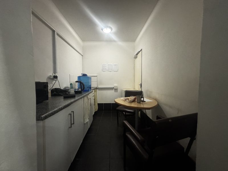 A compact industrial kitchenette featuring built-in cabinetry, laminate countertops, and tiled flooring, suitable for staff breakroom use.