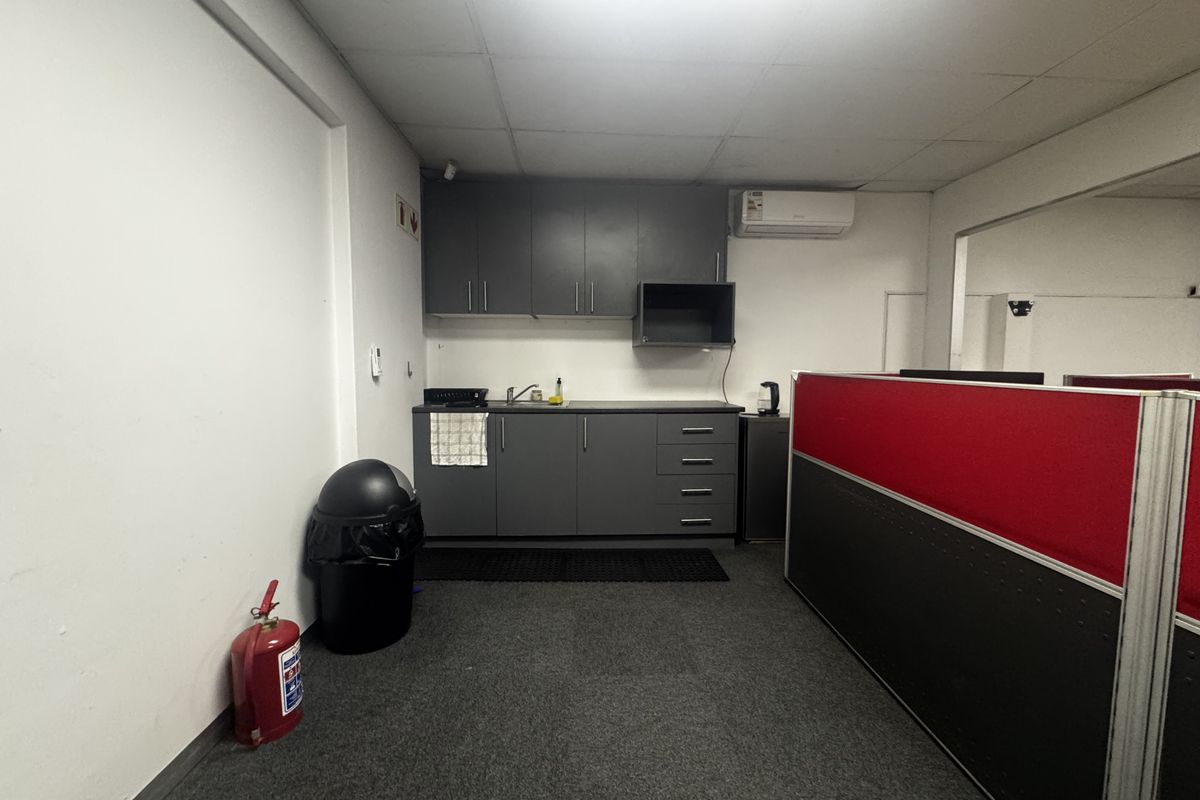 A functional office kitchenette featuring grey built-in cabinetry, a sink, and a wall-mounted air conditioning unit.
