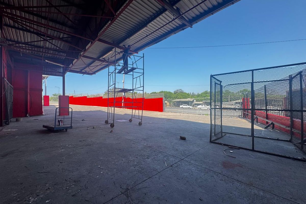 Large industrial covered loading or storage area featuring concrete flooring, steel structural supports, and perimeter security fencing.
